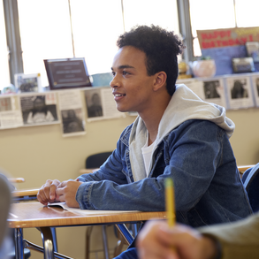 teenage boy student sitting at a desk in a full classroom